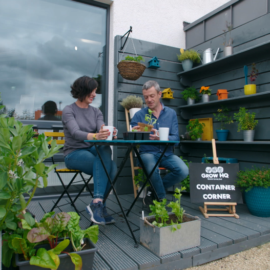 A woman and a man sitting at a table outside surrounded by containers of vegetables