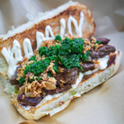 Close-up of a Filipino-style beef sandwich from Bahay, topped with crispy onions, green herb sauce, and mayonnaise on toasted bread.