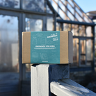 A GROWBox for Kids from GIY placed on a wooden post with a greenhouse in the background.